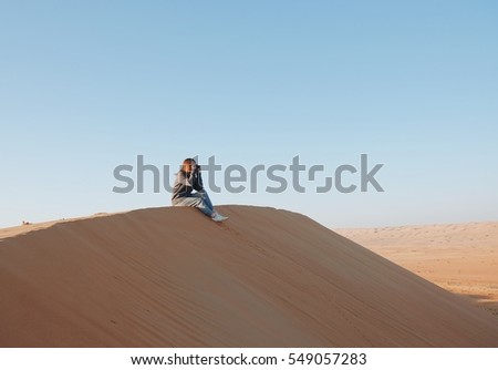 Young woman sitting and taking photo on desert sand in Oman