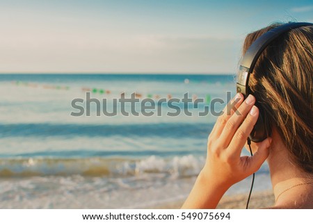 Beautiful young girl in bikini is listening music with headphones on the beach
