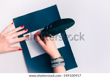 Young woman hands with elegant red nails and glossy wristband writing important old post mail with teal blue goose quill pen - wedding invitation, Valentine card or Dear Santa letter background