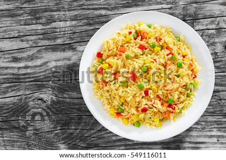 Sweet Corn, red bell pepper, green peas delicious  healthy Risotto on white plate on old wooden table, view from above Royalty-Free Stock Photo #549116011