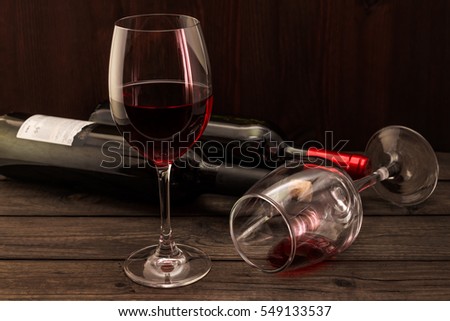 Two bottles of red wine with two glasses on an old wooden table. Focus on an overturned glass of wine