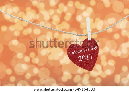 Red Heart hung on hemp rope and have text Happy Valentine's Day 2017 on abstract Orange color of boken background.
