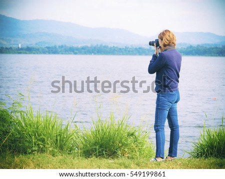 Side view of young woman photographer holding camera in green nature