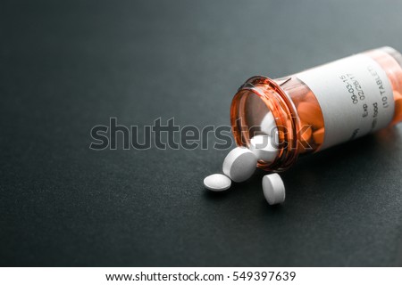 White pills spilling out of a toppled bright red orange pill bottle Royalty-Free Stock Photo #549397639