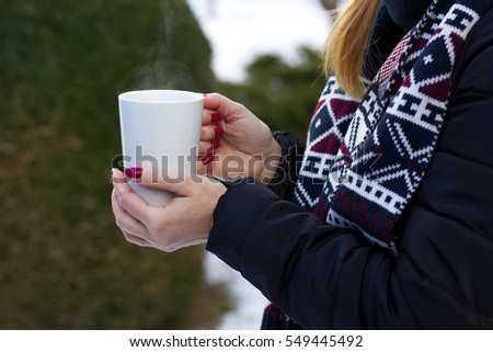 woman holding a hot cup of coffee in her hands outdoors in winter, numbed female hands with polished nails 