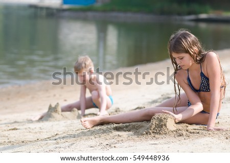 Eleven years girl pretty girl plays with sand on the beach with her brother on background