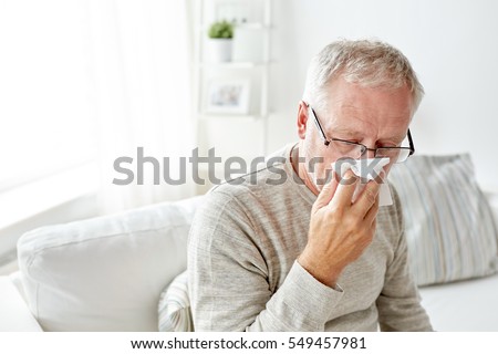 healthcare, flu, hygiene and people concept - sick senior man with paper wipe blowing his nose at home Royalty-Free Stock Photo #549457981