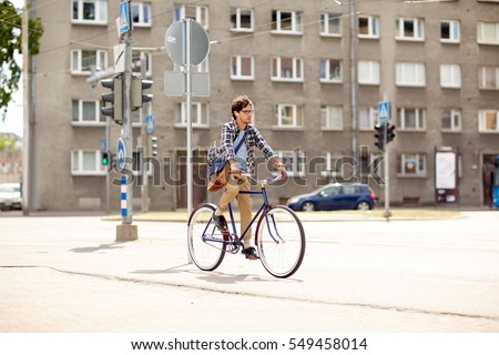 people, style, leisure and lifestyle - young hipster man with shoulder bag and earphones riding fixed gear bike on city street