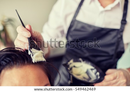 beauty and people concept - close up of stylist with hair dye and brush coloring hair at salon Royalty-Free Stock Photo #549462469