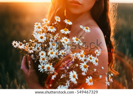 in front of the sun girl holding a bouquet of daisies, rays of sunset Royalty-Free Stock Photo #549467329