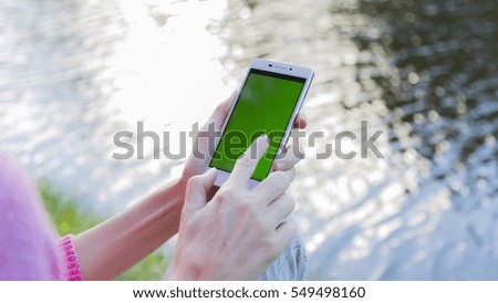 The smartphone in the hands of a young woman near the lake