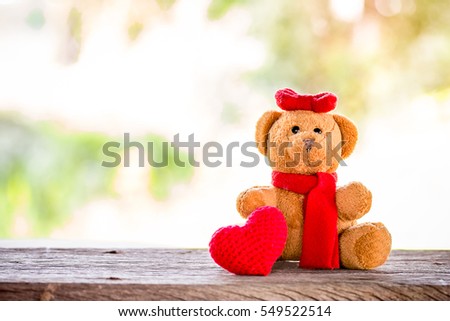 valentine day decoration with brown bear and red heart knitting shape on wooden mock up over blurred green garden on day noon light,Image for Happy Valentine holiday concept.