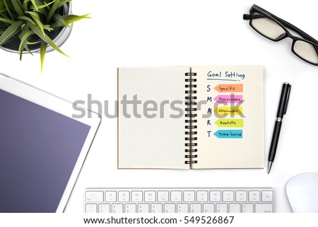 Smart goal setting with notebook, eye glasses, pen, mouse, keyboard, tablet, computer and plant on white office table view from above, Success concept