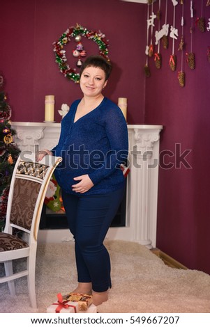 A pregnant woman. Photo studio near the fireplace. Christmas motif.