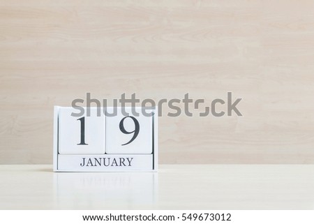 Closeup surface white wooden calendar with black 19 january word on blurred brown wood desk and wood wall textured background with copy space , selective focus at the calendar