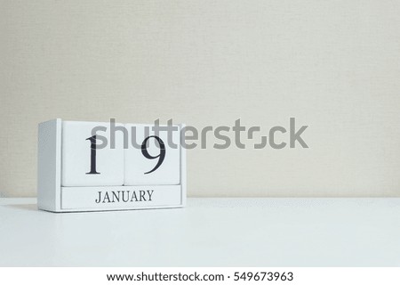 Closeup white wooden calendar with black 19 january word on blurred white wood desk and cream color wallpaper in room textured background with copy space , selective focus at the calendar
