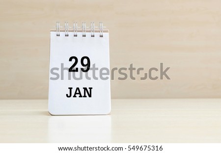 Closeup surface note book with black 29 jan word in page on blurred brown wood desk and wood wall textured background with copy space under window light