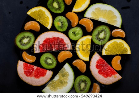 shredded bright vivid brilliant yellow green orange red grapefruit lemon orange Mandarin kiwi sweetie in a black plate on black background close-up