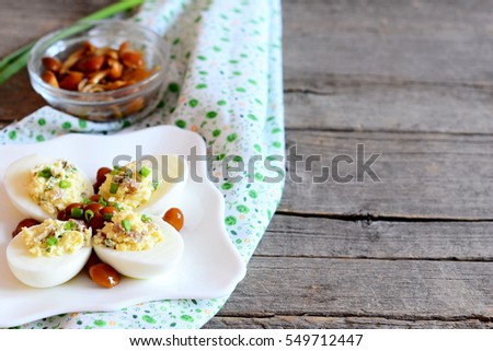 Delicious deviled eggs on a plate. Boiled eggs stuffed with grated cheese, marinated mushrooms and fresh green onions. Simple vegetarian appetizer. Wooden background with blank place for text