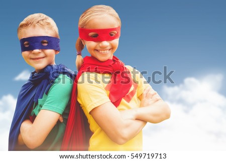 Happy brother and sister in cape and eye mask against blue sky