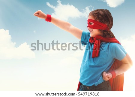 Happy boy in red cape against blue and yellow sky