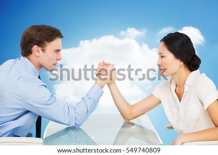 Business couple arm wrestling at desk against cloudy sky