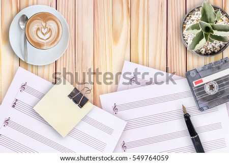 Sheet music, cactus, fountain pen, tape cassette and coffee latte on wooden table