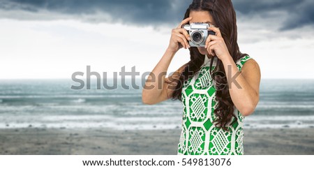 Asian woman taking picture with digital camera against cloudy landscape background