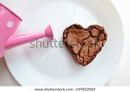 Chocolate chip cookie in the shape of heart, with a watering can on white plate. Concept about love and relationship. (Love growth concept)