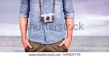 Hipster man holding digital camera against beach scene