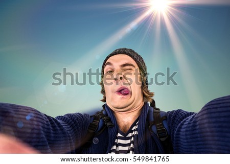 Hipster holding camera and grimacing against blurred mountains