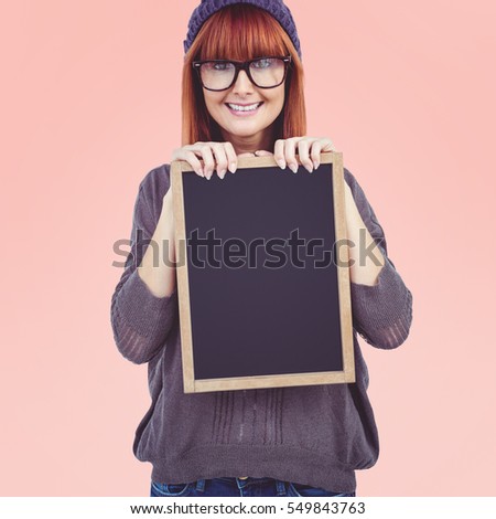Smiling hipster woman holding blackboard against pastel pink