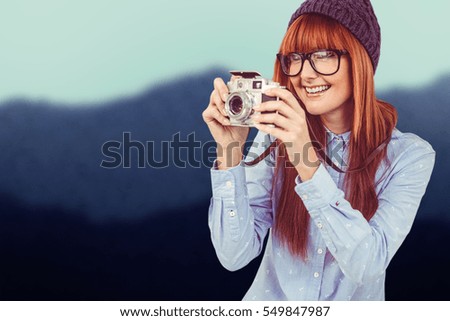Smiling hipster woman taking pictures with a retro camera against blurred mountains