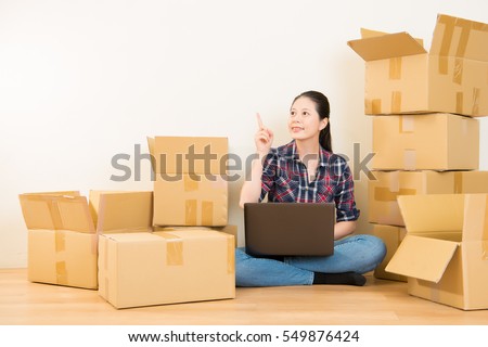 woman got new solutions for apartment decoration sitting on the floor of new apartment, planning redecoration and searching for ideas on laptop computer in home decorating. mixed race asian chinese