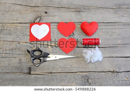 How to hand sew a felt heart for Valentineâ??s day. Tutorial. Red felt heart, cut felt pieces in shape of a heart, synthetic filler, paper template, scissors, thread, needle on a wooden table. Top view