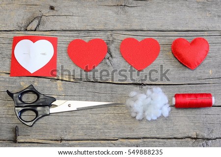 Red felt heart, cut felt parts in shape of a heart, paper pattern, scissors, thread, needle on a wooden table. Felt heart craft for Valentineâ??s day gifts and decorations. Instruction. Top view