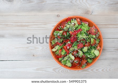 Fresh salad with pepper, avocado and tomato in an orange plate on a wooden table. Rustic style