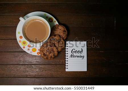 A cup of hot chocolate and a chocolate chip cookies isolated on a rustic wooden background. A notebook with a simple words to make your day ahead
