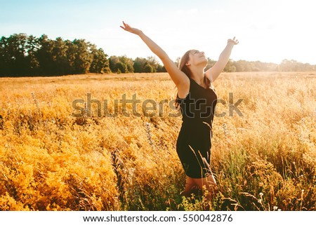 Girl stretching his arms to the sky in a yellow field, sunny summer evening Royalty-Free Stock Photo #550042876