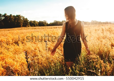 at sunset young girl touching flowers in the yellow field, enjoyment, outdoor recreation Royalty-Free Stock Photo #550042915