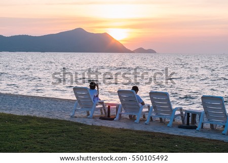 People laying on beach chairs against a beautiful sunset in the sea, Thailand