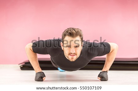 Portrait of a young handsome man doing pushups on fists in a gym.