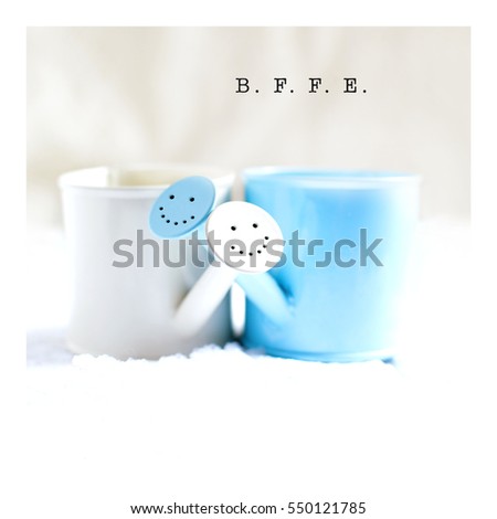 Unusual concept image for Valentines Day. Two cute miniature watering cans with beaming smiles snuggled together with generous accommodation for copy space. Square crop format.
