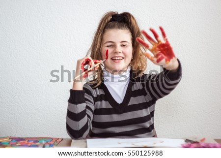 Girl painting with brush and colorful paint with smeared face and hands color
