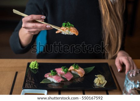Woman eating sushi in the black plate on a wooden table. Hands of the girl close-up.
