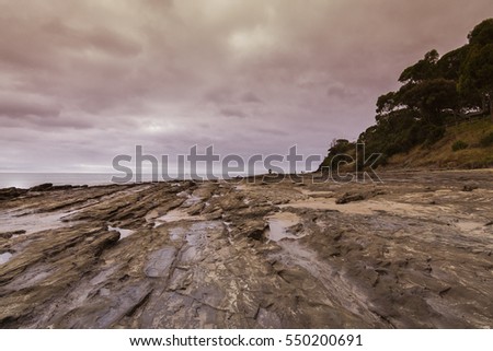 Rocks in the beach with moving rainy purple grey clouds.