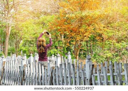 Blond hair woman taking selfie with smart phone on wood bridge in the city park. Lady in the autumn garden .