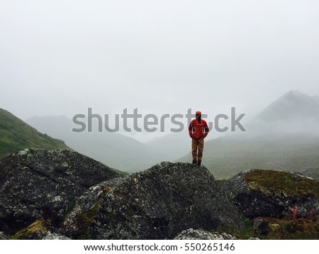 A man stands alone on a boulder in the misty mountains. Royalty-Free Stock Photo #550265146