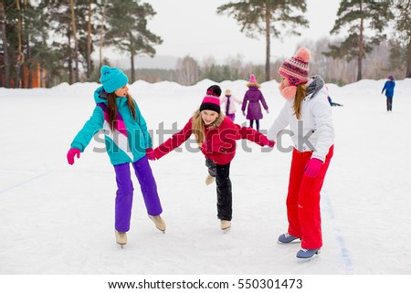 three attractive skater girl on the ice of the frozen lake with kids on the background