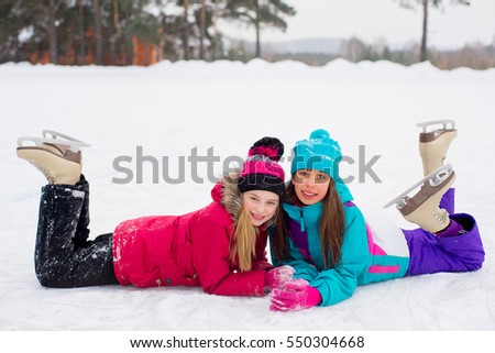 two attractive skater girls lying on the ice of the frozen lake. forest on the background